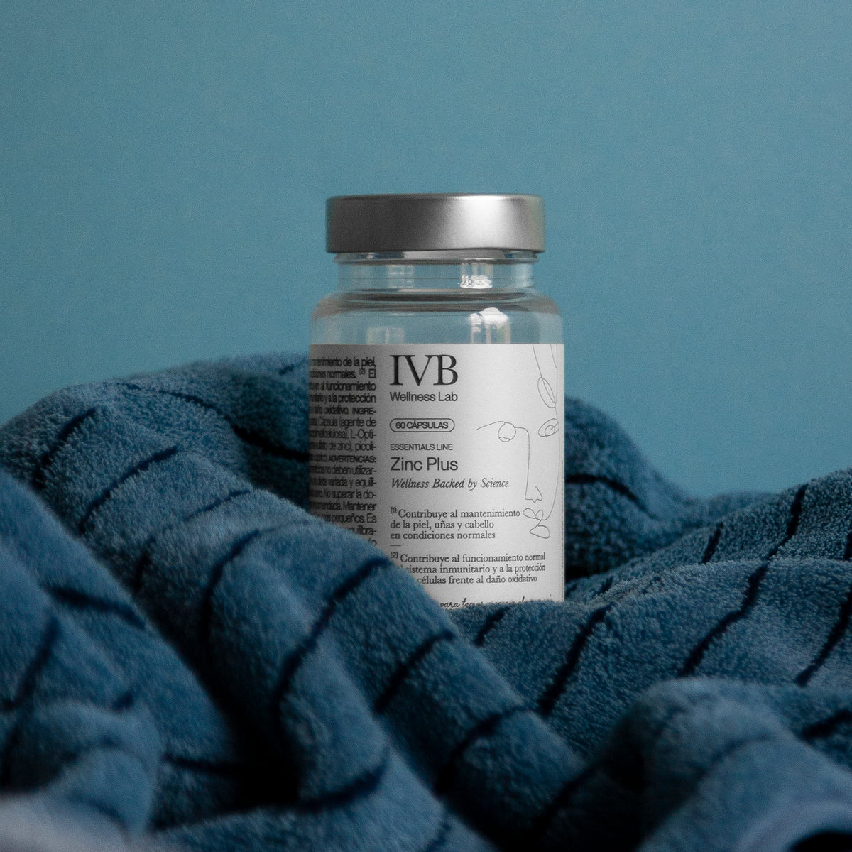 Bote de Zinc Plus de IVB Wellness Lab entre los pliegues de un tejido azul.